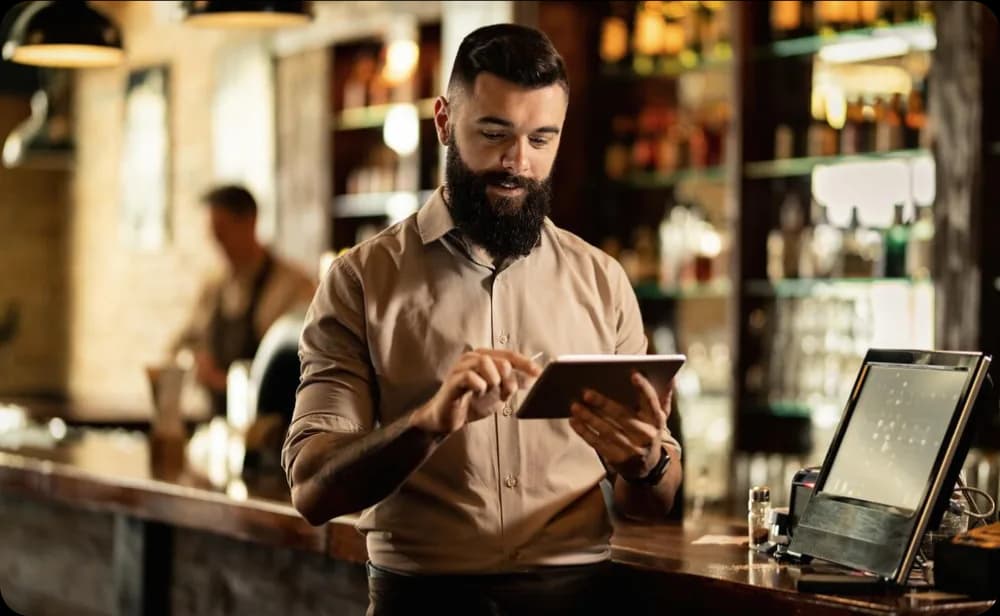 Restaurant manager using a digital tablet at a bar counter to manage daily business operations with Eatsy Orders support.