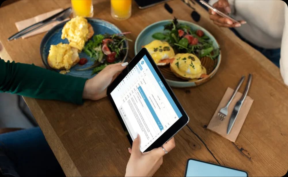 Restaurant owner using a digital tablet at a dining table to make real-time menu and price updates through the Eatsy Orders dashboard.